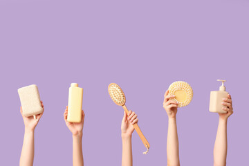 Female hands with bottles of cosmetic products, bath sponges and massage brush on purple background