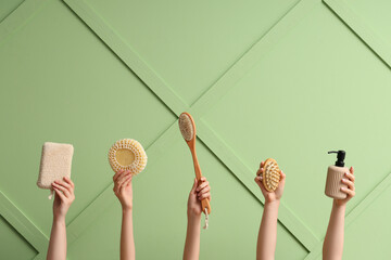 Female hands with bottle of cosmetic product, massage brushes and bath sponges on green background