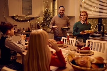 Happy parents serving food for Christmas family dinner at dining table.