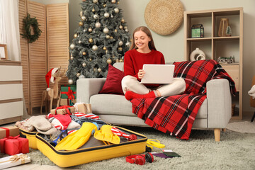 Female traveler using laptop while packing suitcase at home on Christmas eve © Pixel-Shot
