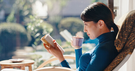 Reading, relax and Asian woman with book, morning and knowledge with literature, coffee and weekend. Home, tea and person with novel, rest and comfortable with story, break and cozy on chair or Japan