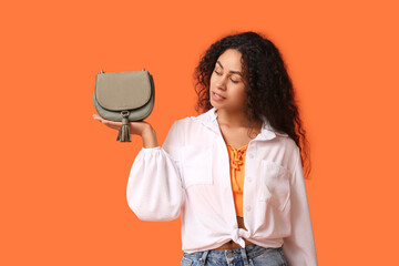 Beautiful young African-American woman with stylish grey bag on orange background