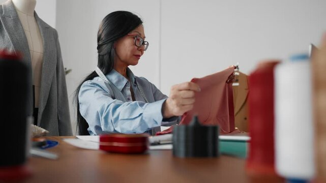 Chinese dressmaker in fashion atelier, aged lady choosing tissues for clothes. Portrait of senior designer lady creating new clothes in her own working studio, profession and creative hobby, hand-made