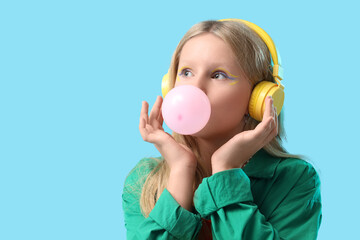 Cute trendy girl in headphones blowing bubble gum on blue background
