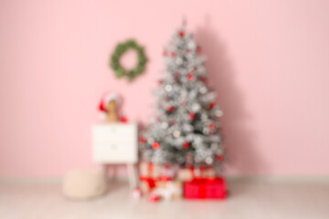 Decorated Christmas tree, gifts and wreath on pink wall in room. Blurred view