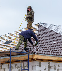 Two men are working on a roof, one of them is using a tape measure