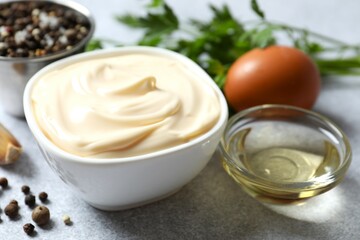 Bowl with mayonnaise and ingredients for cooking on gray background
