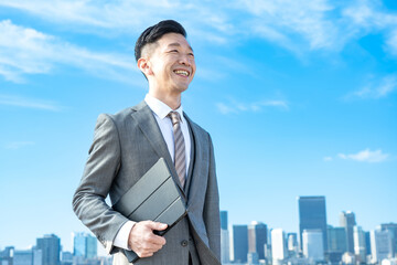 青空とビル群を背景にしたビジネスマンのポートレート