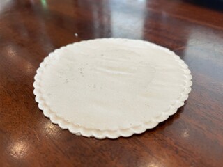 A Close-Up View of a White Scalloped-Edge Coaster Resting on a Polished Wooden Surface
