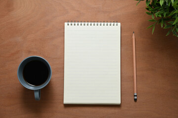Blank notepad, pencil and a cup of coffee on wooden desk for starting a productive day of writing...