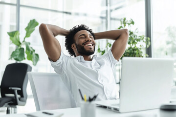 man is sitting at a desk with a laptop and smiling. He is relaxed and enjoying his time