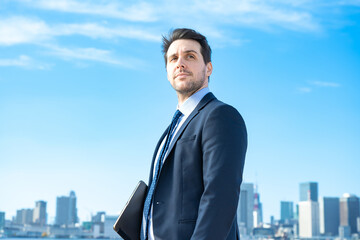 青空とビル群を背景にしたビジネスマンのポートレート