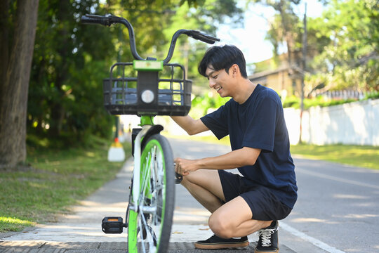 Young asian man inspecting a bicycle before riding in public park
