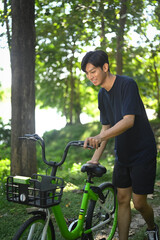 Obraz premium Smiling young man walking with his bike through tree lined path
