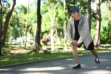 Motivated young sportsman stretching his leg preparing for a workout outdoors in the park