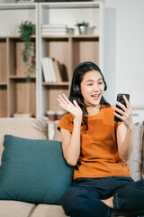 Obraz premium Happy woman having fun doing video call using mobile phone and Laptop sitting on sofa, home office workplace lifestyle people.
