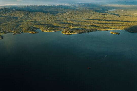 A small plane flies over a lake at sunset.