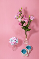 Meringue in a glass on a pinc background. Desserts. Sweets. Vase with pink flowers. Two small cups