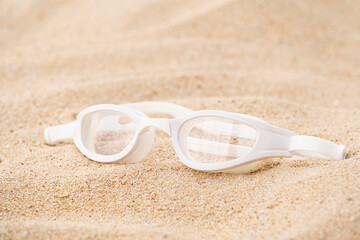 white swimming glasses on sandy beach background