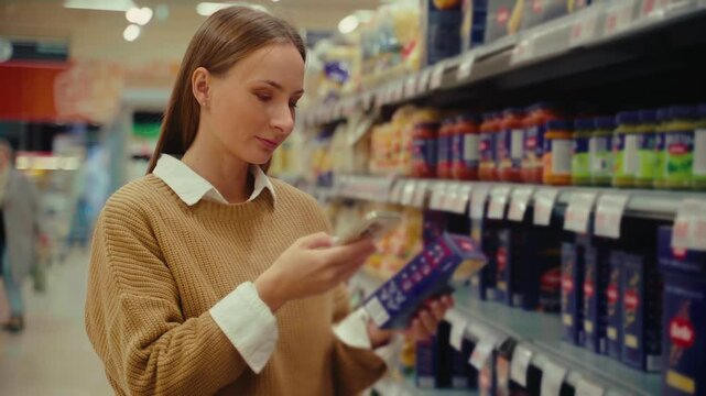 A woman diligently scans products while shopping in a supermarket, ensuring she keeps track of her purchases and finds the best deals during her grocery run.