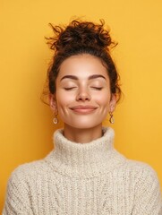 Happy calm patient young woman makes zen nirvana gesture meditates with closed eyes practices yoga has combed hair wears earrings and casual jumper smiles happily isolated over yellow background.
