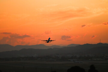 Airplane takeoff, soaring towards the vibrant horizon of a red and orange sunset, with majestic mountains in the background. A breathtaking scene perfect for promoting travel and holidays