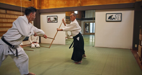 Dojo, class and teacher at Aikido training in gym with wood sword Japanese martial arts and fight...
