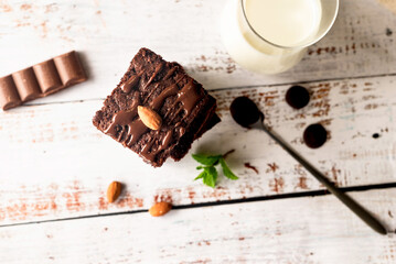 Chocolate brownies with melted chocolate topping, almond and leaves mint with glass of milk on table.