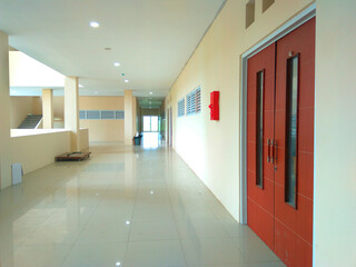 A long narrow corridor with a tiled floor, white walls, and a red door at the end. The corridor is...