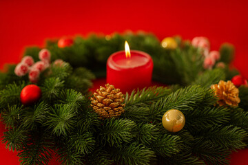 Festive holiday scene featuring glowing candles, evergreen branches, golden pinecones, and red ornaments on a bold red backdrop