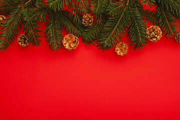 red christmas background. Minimalist Christmas arrangement with fresh evergreen branches and golden pinecones on a vibrant red background, perfect for holiday designs.