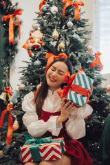 Christmas Cheer: A young woman beams with delight, surrounded by festively wrapped presents near a beautifully decorated Christmas tree.  The scene exudes warmth, joy.