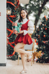 Christmas Cheer: A woman in a red dress holds a wrapped gift, radiating joy and festive spirit in a heartwarming Christmas scene.