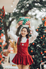 Christmas Cheer: A young woman beams with holiday joy, balancing a festively wrapped gift above her head amidst twinkling Christmas trees.  A delightful image capturing the spirit of the season. 