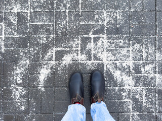 Anti-icing chemicals in winter season. Top view of winter boots and road strewn with technical salt or reagents to prevent icing. Effective tool to fight ice on surfaces. Rock salt on road. 