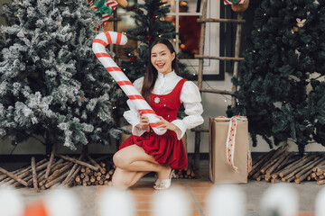 Christmas Cheer with Giant Candy Cane: A young woman in a festive red dress kneels amidst Christmas...