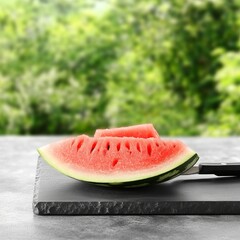 Juicy watermelon slice on slate board, outdoors.