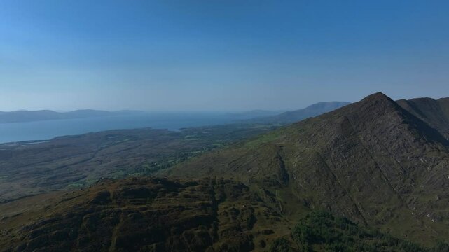 Sugarloaf, Caha Mountains, County Cork, Ireland, September 2024. Drone pulls backwards above the craggy peaks with the rugged landscape of Trafrask and the North Atlantic Ocean in the background.