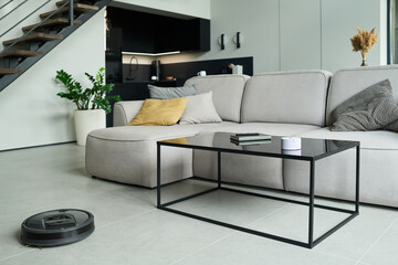 Modern minimalist living room featuring a sectional sofa, glass coffee table, and potted plant near the staircase. Clean lines and neutral colors emphasize contemporary aesthetics