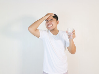 Handsome young man over grey grunge wall drinking glass of water stressed with hand on head, shocked with shame and surprise face, angry and frustrated.