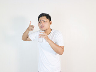 Young asian man hold glass of water and gesture smell isolated. guessing a smell