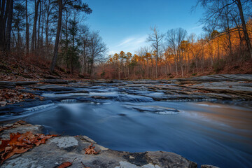 Naklejka premium Scenic view of river flowing through forest with colorful autumn foliage and rocks. Wild mountain cascade river with stones