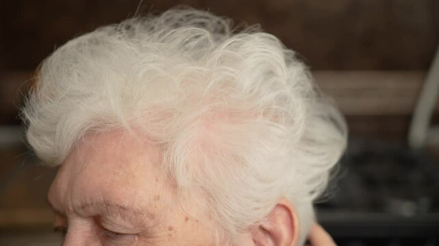 Old woman touches hair with hand close up. Elderly female dyed gray hair. Senior woman runs hand over head. Flabby and wrinkled skin on senior female face