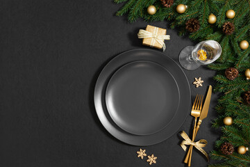 Beautiful Christmas table setting with black empty plate, gold accessories and fir branches on a black background with copy space. Top view, flat lay.