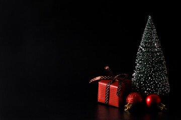 Miniature Christmas tree with red present box on black background.