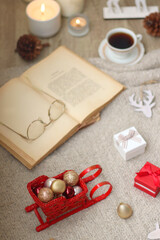 Various Christmas decorations, lit candles, cup of tea or coffee, cookies, books, presents and soft blanket on the table. Holiday hygge at home. Selective focus.