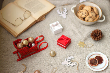 Various Christmas decorations, lit candles, cup of tea or coffee, cookies, books, presents and soft blanket on the table. Holiday hygge at home. Selective focus.