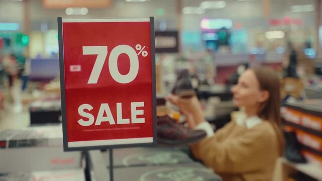 Shoppers explore a retail store with significant discounts. A woman examines shoes while a vibrant sale sign highlights a 70 percent reduction on prices, attracting eager buyers.