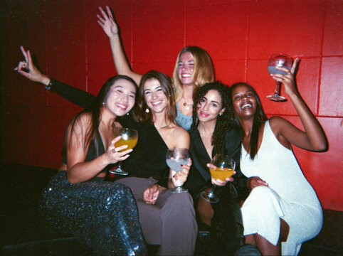 A group of friends enjoy a fun night out, holding drinks and celebrating together. The photograph has been done with a film camera, giving it a vintage, dusty look. - Powered by Adobe