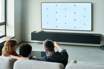 Group of people sitting on a stylish couch, engaged in watching a television with a minimalist...